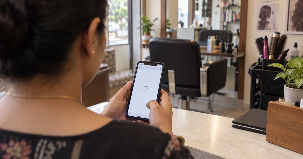 A salon owner checks a loading webpage on a phone at the reception counter.